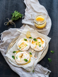 Merengues with lemon curd and fresh mint on silver tray, beige kitchen towel and grunge dark background